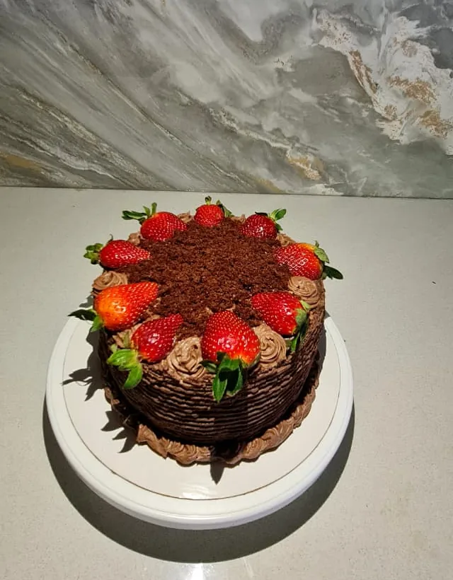 Chocolate strawberry cake on a white cake stand against a marble backsplash
