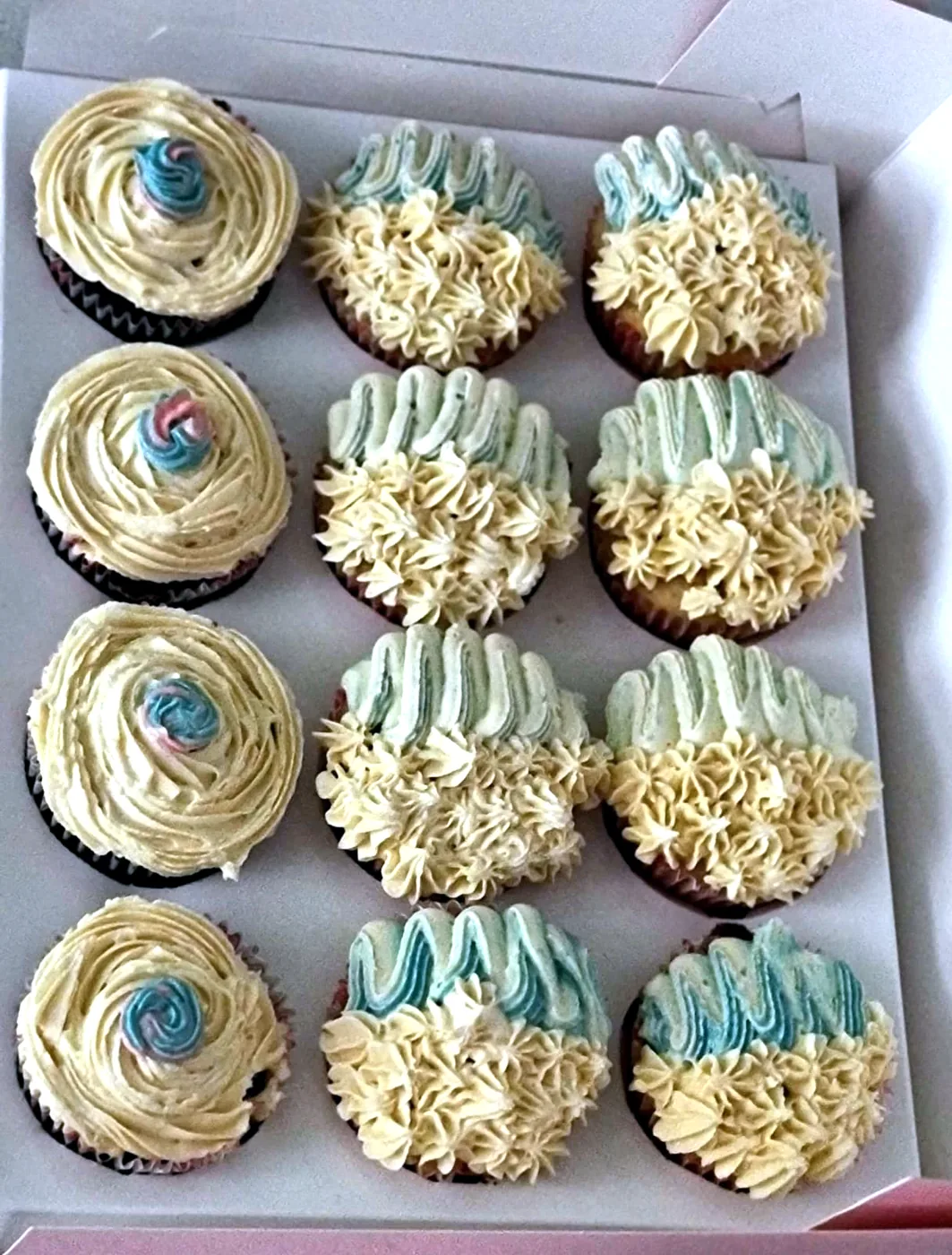 Box of cupcakes with cream swirls and pastel blue piping