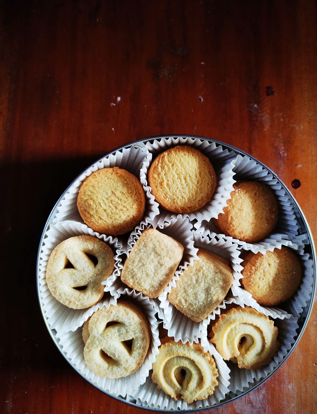 Round tin of assorted butter cookies on a wooden table