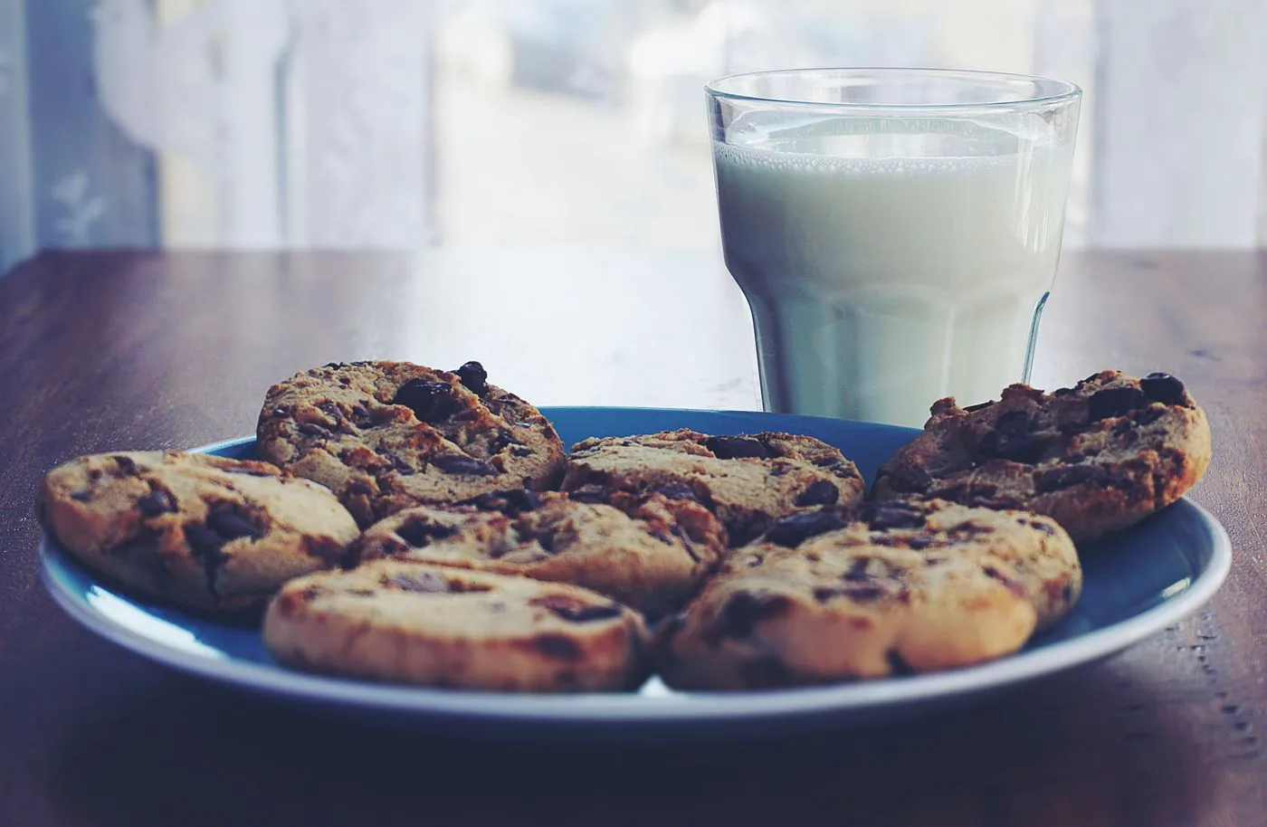 Chocolate chip cookies on a blue plate with a glass of milk