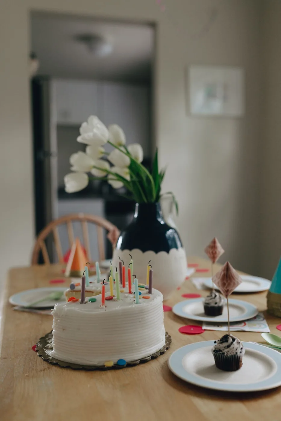 Dining table set with a celebration cake, cupcakes and flowers